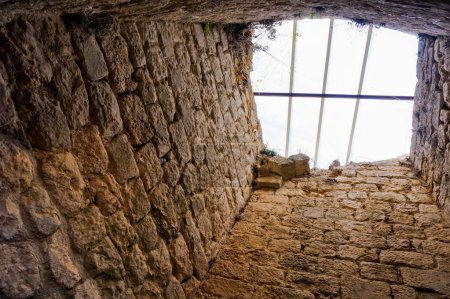 Téléchargez les photos : Castelnau-de-Lvis, France - Février 2020 - Vue en angle bas d'un puits de lumière à l'intérieur des ruines du château médiéval, avec des murs épais et une fenêtre de toit barrée, avec de l'herbe sauvage poussant sur la pierre - en image libre de droit