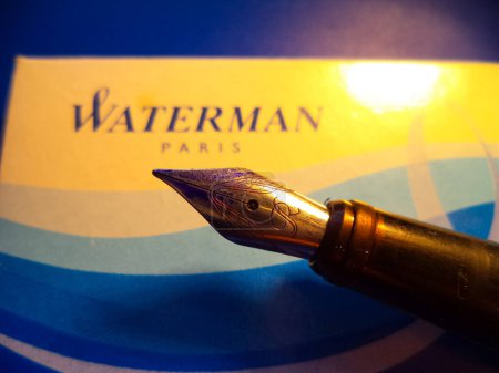 Photo for A LED lamp in the domed form of a cupola radiating yellow light illuminates an old metal fountain pen that features a worked golden nib with stains of blue ink, in warm colors with a dark background - Royalty Free Image