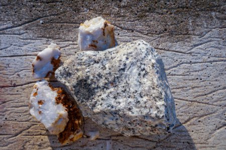 Photo for Crystals on a block of white granite with black spits, flanked by blocks and shards of white quartz with red oxydes at the surface, on a concrete ground - Royalty Free Image