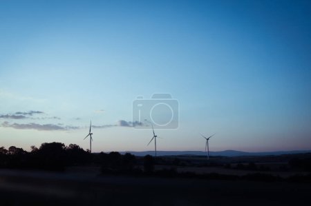 Téléchargez les photos : Un groupe d'éoliennes alignées à l'horizon dans un parc éolien, avec des champs au premier plan, coucher de soleil - en image libre de droit