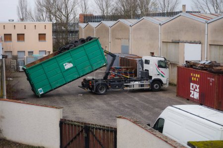Téléchargez les photos : Occitanie, France - Février 2021 - Un camion Volvo de la société française de recyclage Aliapur, chargeant un seau vert amovible chargé de pneus en caoutchouc usagés, dans la cour d'un centre de stockage - en image libre de droit