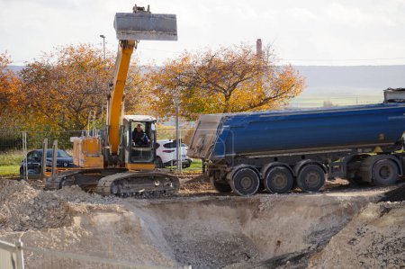 Foto de Reims, Francia - Nov. 2022 - Una excavadora amarilla del fabricante suizo-alemán Liebherr cava un agujero y descarga la tierra en un semirremolque volquete, en una obra de construcción en el campus URCA - Imagen libre de derechos