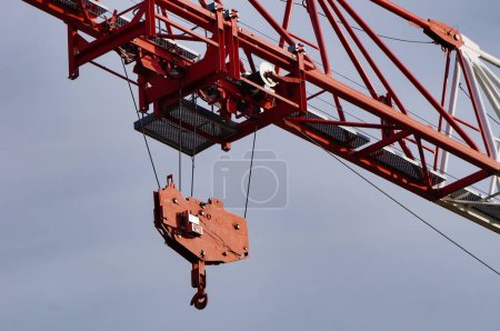 Photo for Detail of a construction crane on a work site, featuring the steel hook to lift the load and the pulley system linked with cables to the mobile carriage, which is mounted on tracks on the main boom - Royalty Free Image