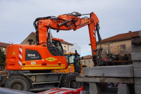Foto de Villefranche d 'Albi, Francia - Feb. 2021 - Una excavadora 914 Compact naranja, con ruedas, fabricada por el fabricante suizo-alemán Liebherr, estacionada en medio de materiales de construcción, en una obra de construcción - Imagen libre de derechos