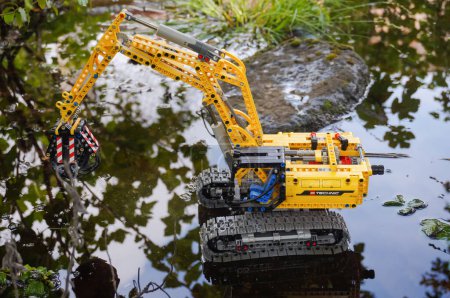Photo for Occitanie, France - May 2020 - Scale model (child's toy) of a tracked excavator equipped with a hydraulic grapple attached to the mechanical arm, operating in the water in a wild marshland landscape - Royalty Free Image