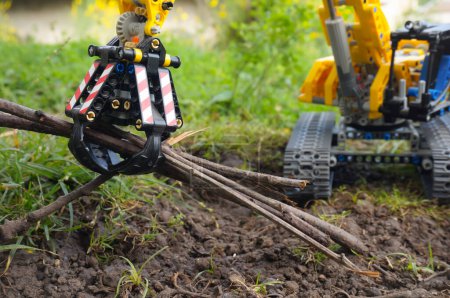 Photo for Scale model (a Lego child's toy) of a yellow tracked excavator turning on its chassis, in a garden - Royalty Free Image