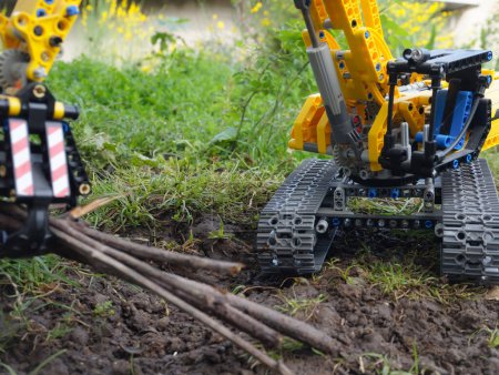 Foto de Modelo a escala (juguete de niño Lego) de una excavadora de orugas amarillas que gira sobre su chasis, en un jardín - Imagen libre de derechos