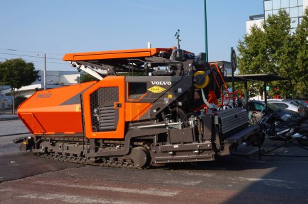 Photo for Gennevilliers, France - Sept. 2020 - An orange track-laying P6820D ABG asphalt paver, manufactured by the Swedish company Volvo and operated by the French construction group Colas (Bouygues) - Royalty Free Image