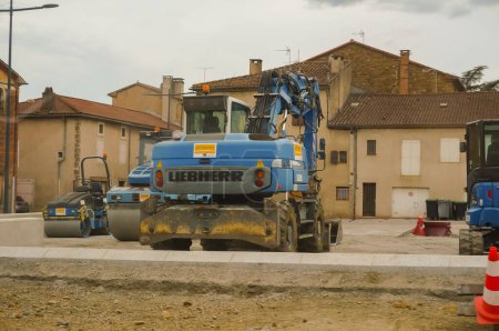 Téléchargez les photos : Realmont, France - Août 2020 - Une excavatrice à roues bleues fabriquée en France par le fabricant germano-suisse Liebherr, des rouleaux à vapeur et une mini-pelleteuse, sur un chantier de construction sur une place de la ville - en image libre de droit