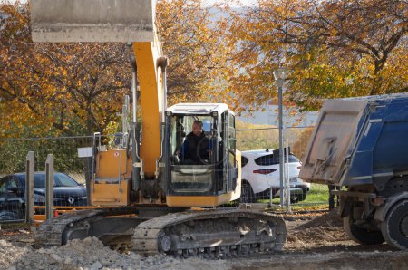 Téléchargez les photos : Reims, France - Novembre 2022 - Un travailleur exploite une excavatrice mécanique jaune du fabricant germano-suisse Liebherr, sur le campus URCA ; à côté de lui, un camion à benne est prêt à évacuer le sol excavé - en image libre de droit