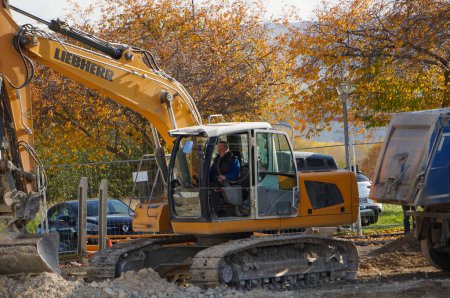 Foto de Reims, Francia - Nov. 2022 - Una excavadora amarilla del fabricante suizo-alemán Liebherr cava un agujero y descarga la tierra en un semirremolque volquete, en una obra de construcción en el campus URCA - Imagen libre de derechos