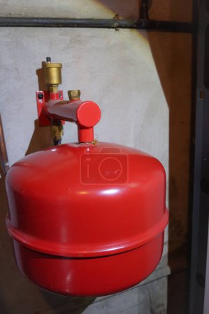 Foto de Depósito metálico rojo de expansión de un sistema de calefacción central, instalado junto a la caldera de gas en el sótano de una casa; está destinado a regular el volumen del fluido que circula dentro del circuito - Imagen libre de derechos
