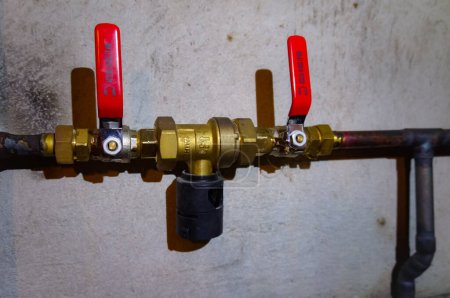 Photo for Tarn, France - Aug. 2020 - Ball valve, with two red flat handles, of the gas supply pipe of a central heating system ; the brass and copper pipe features a polystyrene wrapping for insulation - Royalty Free Image