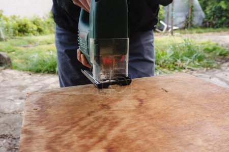 Téléchargez les photos : Tarn, France - Mai 2020 - Travail manuel extérieur et travail de menuisier : un artisan utilise une scie à flèche électrique pour couper une planche de bois en projetant de la fraise et guide la lame en suivant une ligne marquée - en image libre de droit