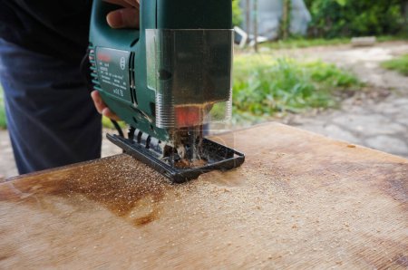 Foto de Tarn, Francia - Mayo 2020 - Trabajo manual al aire libre y trabajo de carpintería: un artesano opera una sierra eléctrica para cortar una plancha de madera proyectando frass y guía la hoja siguiendo una línea marcada - Imagen libre de derechos