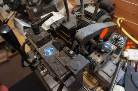 Foto de París, Francia - Sept. 2020 - Detalle de la compleja máquina herramienta en el taller del artesano que trabaja en la industria de calzado o reparación y corte de llaves, con un cartel azul que aconseja el uso de protección ocular - Imagen libre de derechos