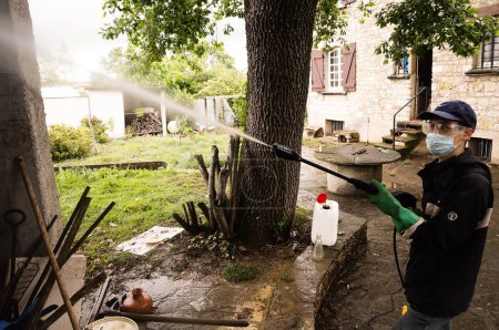 Foto de Tarn, Francia - Mayo 2020- Saneamiento en la ganadería: un trabajador con guantes, gafas de seguridad y máscara desinfecta un gallinero infestado de alimañas rociando pesticida químico con un pulverizador - Imagen libre de derechos