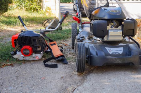 Photo for Albi, France - Aug. 2020 - A brush cutter made in China, designed by the German firm Scheppach, next to a lawn mower motorized by the Japanese manufacturer Honda ; both machines are gas-powered - Royalty Free Image