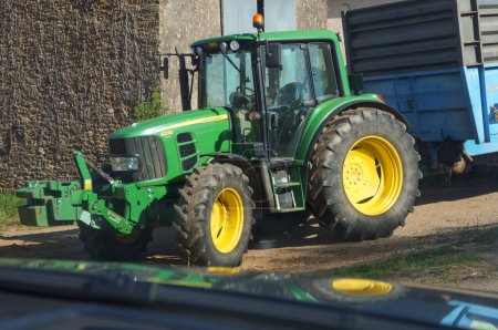 Téléchargez les photos : Tanus, France - Juillet 2021 - Un tracteur John Deere vert et jaune remorque une remorque, dans la zone rurale du Tarn ; John Deere est un fabricant américain qui produit des moteurs en France - en image libre de droit