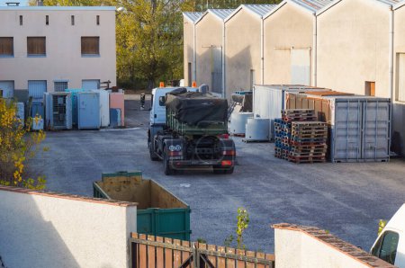 Téléchargez les photos : Tarn, France - Février 2021 - Un camion, après avoir récupéré une benne kaki, quitte la cour d'un centre logistique, où sont stockés des conteneurs maritimes et d'autres marchandises - en image libre de droit