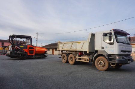 Foto de Tarn, Francia - Feb. 2021 - Equipo de construcción para obras viales en un estacionamiento: un camión volquete Renault blanco de seis ruedas en la vanguardia, y una pavimentadora de asfalto Volvo ABG en el fondo - Imagen libre de derechos