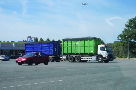 Photo for Albi-Le Sequestre, France - June 2021 - A truck with a removable bucket, towing an additional trailer, from the French waste management company Coved, passes by La Baute commercial center car park - Royalty Free Image