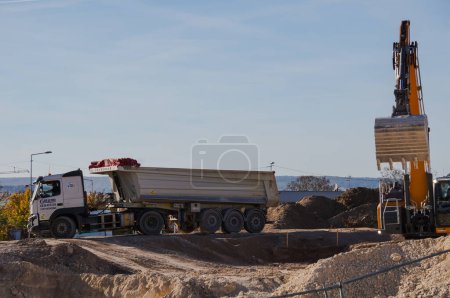 Foto de Reims, Francia - Oct. 2022 - Lugar de trabajo en el campus de ciencias Moulin de la Housse de la URCA: una excavadora Liebherr montada sobre orugas excava cimientos y descarga la tierra en el volquete de un camión de construcción - Imagen libre de derechos