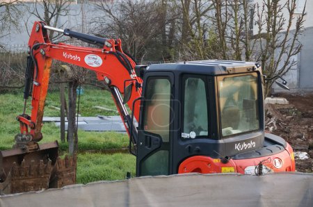 Foto de Tarn, Francia - Feb. 2021 - Cabina del operador, brazo trasero y mecánico de una mini excavadora roja, pequeña y compacta del fabricante japonés de equipos de construcción Kubota, utilizada en un jardín - Imagen libre de derechos