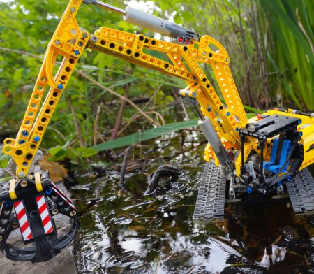 Photo for Occitanie, France - May 2020 - Scale model (child's toy) of a tracked excavator equipped with a hydraulic grapple attached to the mechanical arm, operating in the water in a wild marshland landscape - Royalty Free Image