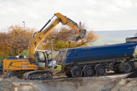 Téléchargez les photos : Reims, France - Novembre 2022 - Une excavatrice jaune du fabricant germano-suisse Liebherr creuse un trou et déverse la terre dans une semi-remorque benne, sur un chantier sur le campus URCA - en image libre de droit