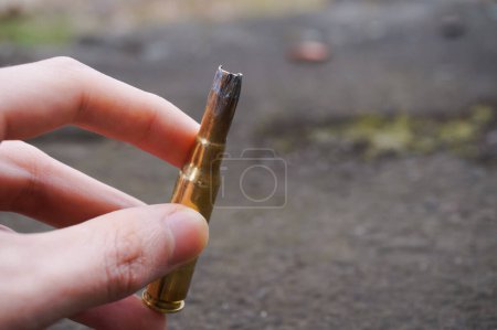 Photo for A hand holding an used 7.62-millimeter caliber cartridge fired during practice shootings by paratroopers of the French Army ; the blackened cartridge head is burnt and distorted by the shotgun - Royalty Free Image