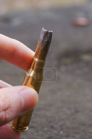 Photo for A hand holding an used 7.62-millimeter caliber cartridge fired during practice shootings by paratroopers of the French Army ; the blackened cartridge head is burnt and distorted by the shotgun - Royalty Free Image