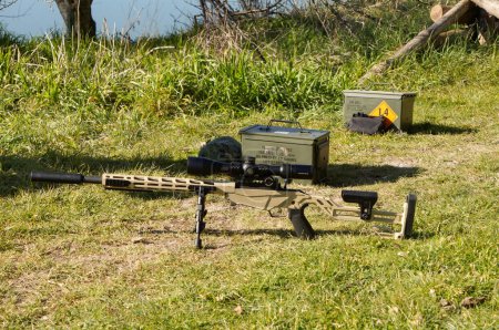 Photo for Occitanie, France - Feb. 2023 - A Ruger Precision Rimfire rifle, mounted on a bipod, is laid in the grass in an outdoor shooting range, with two ammunition boxes containing .22 LR "Winchester" bullets - Royalty Free Image
