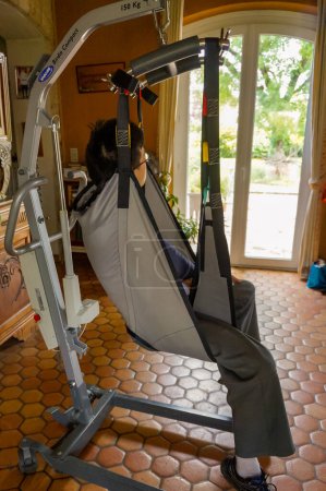 Photo for Occitanie, France - May 2020 - Live demonstration of use of medical equipment for home care : a model installed in a strap hangs on the mechanical arm of an electrical lift for patient transfer - Royalty Free Image