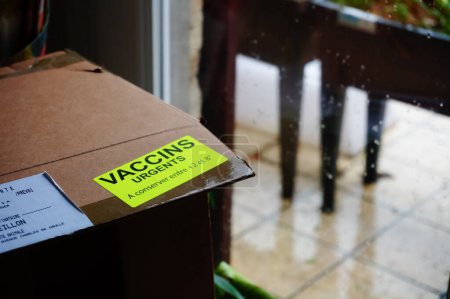 Téléchargez les photos : Occitanie, France - Avril 2022 - Une boîte en carton de vaccins livrés à une pharmacie, avec une étiquette jaune fluorescente marquée "urgent", avec une gamme de températures pour les instructions de stockage - en image libre de droit