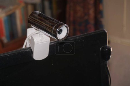 Téléchargez les photos : Webcam externe utilisée pour le télétravail ou la télésurveillance, fixée sur le bord supérieur d'un moniteur d'ordinateur au moyen d'un support avec une pince en plastique, et connectée à celui-ci par un câble USB blanc - en image libre de droit