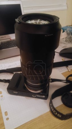 Foto de Tarn, Francia - Dic. 2020 - Una lente de 70-210 mm de largo AF Konica-Minolta orientada verticalmente, fabricada en Japón (teleobjetivo), adaptada en una cámara híbrida Sony Alpha NEX-3N, que se coloca en un escritorio - Imagen libre de derechos