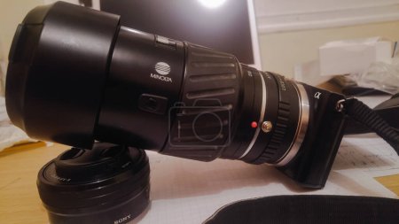 Foto de Tarn, Francia - Dic. 2020 - Equipo japonés de un fotógrafo: una lente de 70-210 mm de largo (teleobjetivo) fabricada por Konica Minolta, fijada a una cámara Alpha NEX, apoyada en una lente Sony de 16-50 mm - Imagen libre de derechos