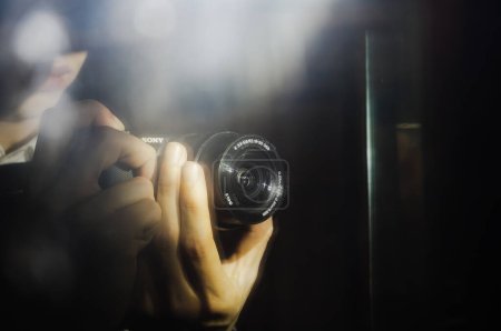 Foto de Tarn, Francia - Feb. 2020 - Imagen borrosa y duplicada en un espejo del objetivo de una cámara híbrida Sony Alpha, sostenida en las manos del fotógrafo, con problemas debido a la luz del flash - Imagen libre de derechos