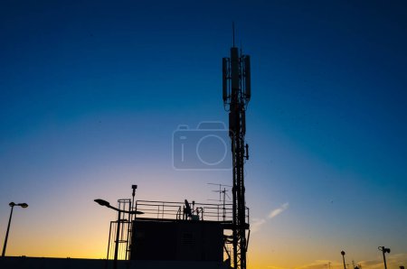 Téléchargez les photos : Silhouette de l'antenne de télécommunication de la station de base installée au sommet du parking de Carmes, qui domine la ville de Toulouse en France, sur fond de ciel bleu foncé au lever du soleil - en image libre de droit
