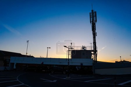 Téléchargez les photos : Silhouette de l'antenne de télécommunication de la station de base installée au sommet du parking de Carmes, qui domine la ville de Toulouse en France, sur fond de ciel bleu foncé au lever du soleil - en image libre de droit