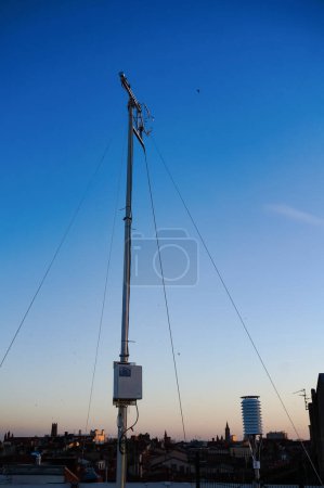 Photo for Steel pole stabilized by cables of the meteorological station settled on top of Carmes car park, featuring sensors for weather measurements and air pollution control, in a blue sky background at dawn - Royalty Free Image