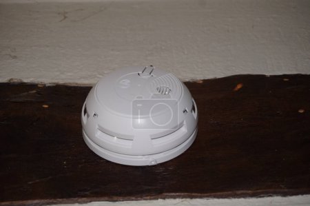 Photo for A round smoke sensor fixed to a timber beam, connected to a remote surveillance system ; such fire prevention systems for homes are mandatory in France, in accordance with legal security requirements - Royalty Free Image