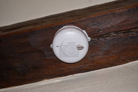 Photo for A classic, standard round smoke detector, fixed to a wooden girder on the ceiling ; such fire prevention systems for homes are mandatory in France, in accordance with legal security requirements - Royalty Free Image