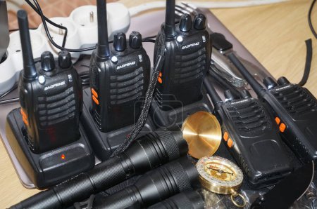 Foto de Occitanie, Francia - Dec. 2021 - Algunas fuerzas policiales de equipos de supervivencia: una estación de radio con varios walkie talkies en sus muelles de carga, luces de destello metálicas y una brújula con un estuche dorado - Imagen libre de derechos