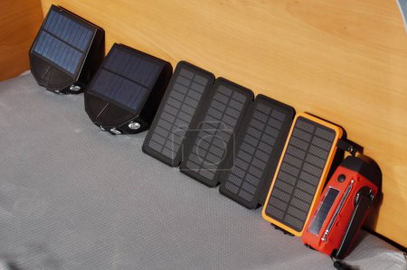 Foto de Un conjunto de dispositivos eléctricos equipados con paneles fotovoltaicos para cargar con energía solar: dos proyectores exteriores led, un banco de potencia móvil con paneles plegables y una antorcha de luz - Imagen libre de derechos