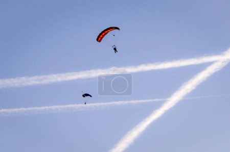 Téléchargez les photos : Deux parachutistes font du parachutisme dans un ciel bleu clair, avec des traînées de jet comme arrière-plan, se préparant à atterrir à l'aéroport d'Albi-Le Sequestre, en France - en image libre de droit