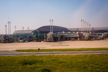 Foto de Roissy, Francia - Junio 2019- Terminal aérea en el aeropuerto de París-Charles de Gaulle, con ventanales de cristal y una arquitectura curvada, con puentes de embarque en el asfalto e iluminadores montados en mástil - Imagen libre de derechos