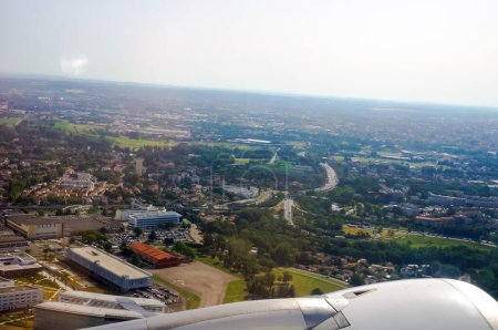 Foto de Motor de una aeronave despegando y ganando altitud en primer plano y vista aérea de áreas industriales, suburbios y carreteras en Toulouse, Francia, con campos y paisaje rural en el horizonte - Imagen libre de derechos