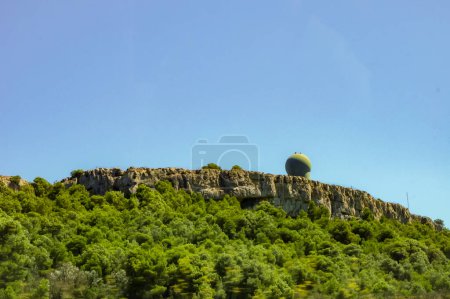 Foto de Narbonne, Francia - Agosto de 2020 - En la cima de acantilados rocosos que sobresalen sobre el macizo arbolado de La Clape, la cúpula esférica del radar para la defensa aérea en las instalaciones militares Roques de la Fuerza Aérea Francesa - Imagen libre de derechos